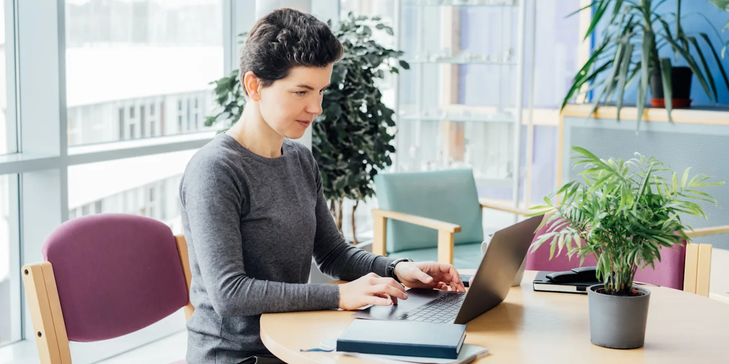 A smiling professional upskilling for advancement, working on a laptop in a modern office.