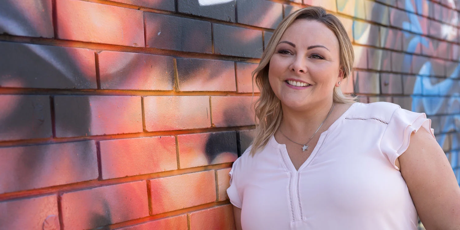 Criminal justice student smiling in front of a bright graffiti piece.