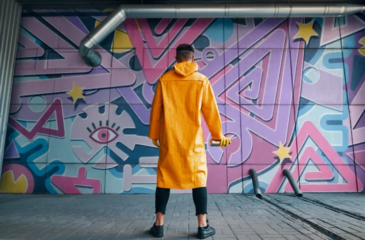 A mural artist standing in front of their graffiti with a spray can in their hand