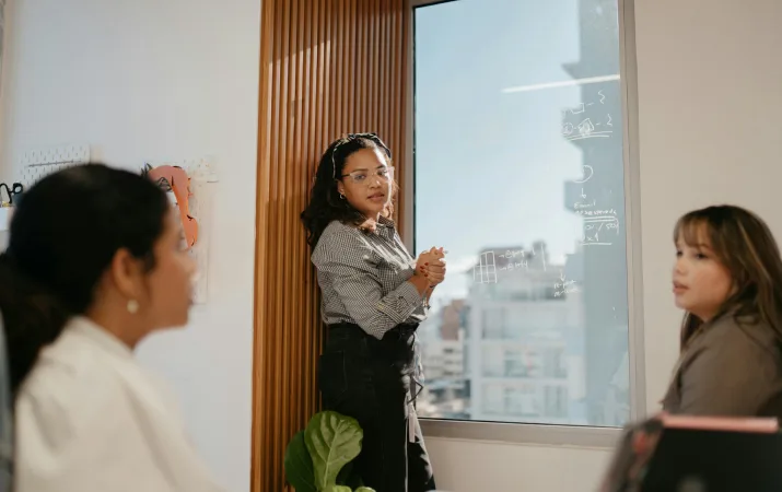 Person presenting handwritten notes on a glass board to a small group.