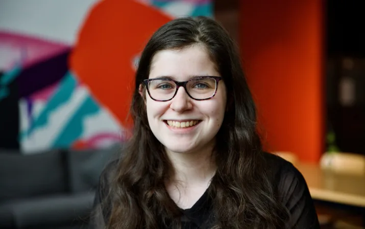 Happy brunette woman with glasses standing in front of an office mural