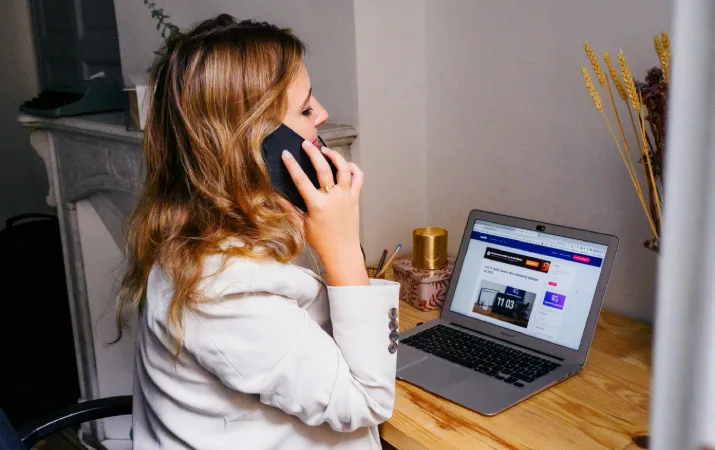 Woman speaking on phone while browsing something on laptop