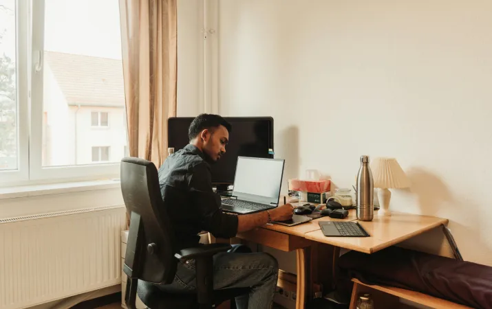 Online student writing notes at his desk in a bright home office