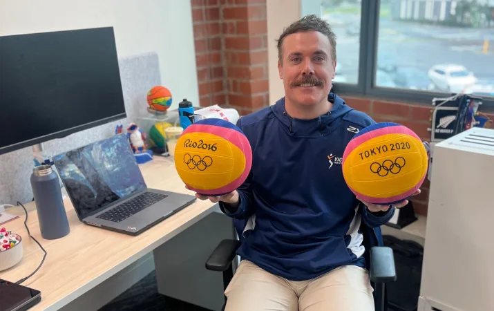 Mat Harris, Performance Science Assistant Manager at the VIS, seated at a workstation, holding a plush Olympics toy ball in each hand.