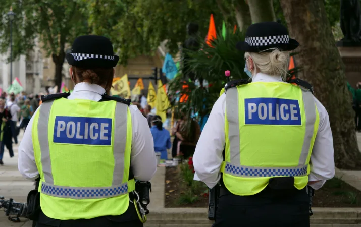 Two female police officers in vests face away looking at crime scene