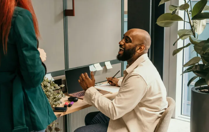 An exuberant social worker chatting to a colleague at his desk