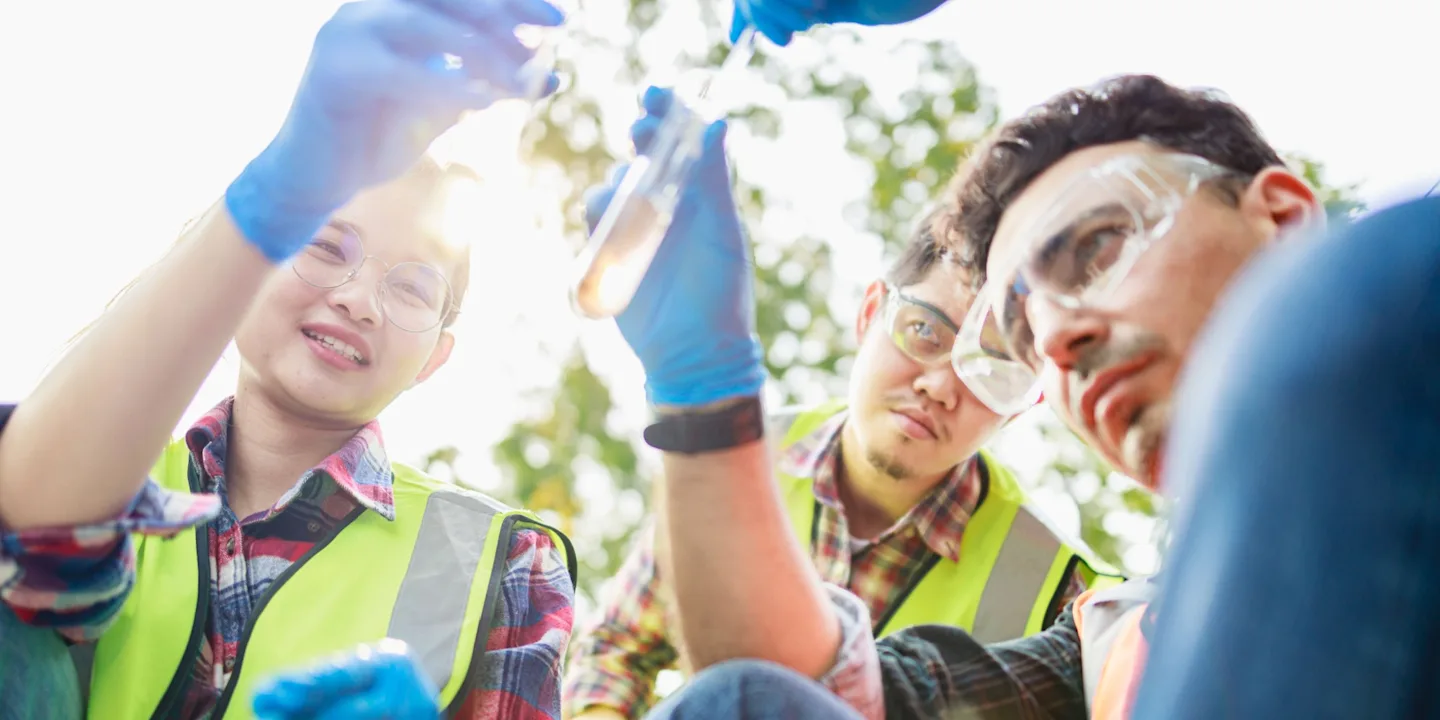 A team of scientists taking water samples in a leafy and sunny outdoor location.