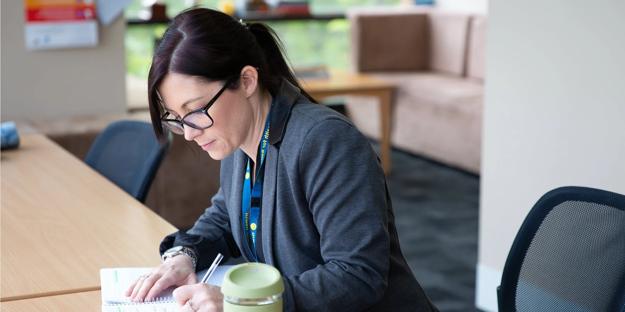 A postgraduate student drinking coffee and scheduling in her diary in a bright and modern workplace.