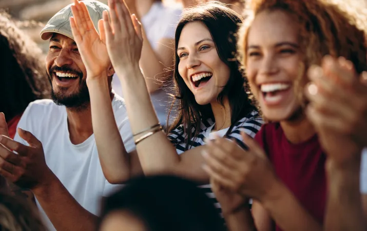 Three people cheering and clapping while looking at something in the distance