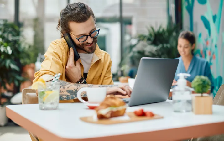 Man submitting documents over laptop while smiling and chatting on phone