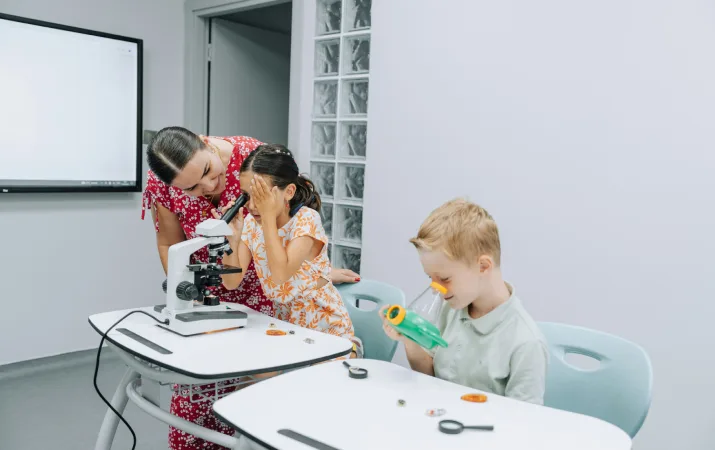 A student teacher and two primary school students learning with a microscope 
