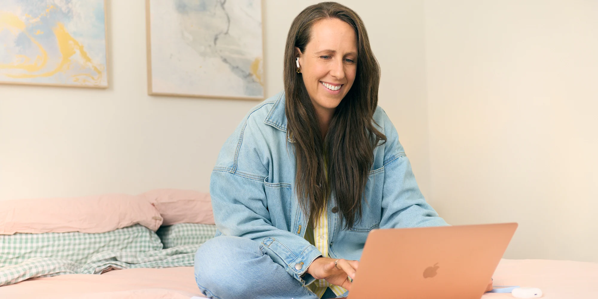 Smiling woman wearing AirPods studies on her laptop at home, focused and relaxed.