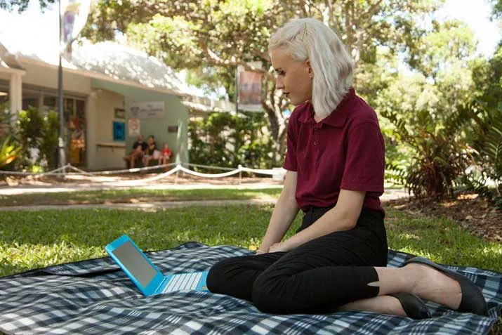 Open Universities Australia student Josephine, set up to study on a picnic blanket with a laptop computer outdoors.