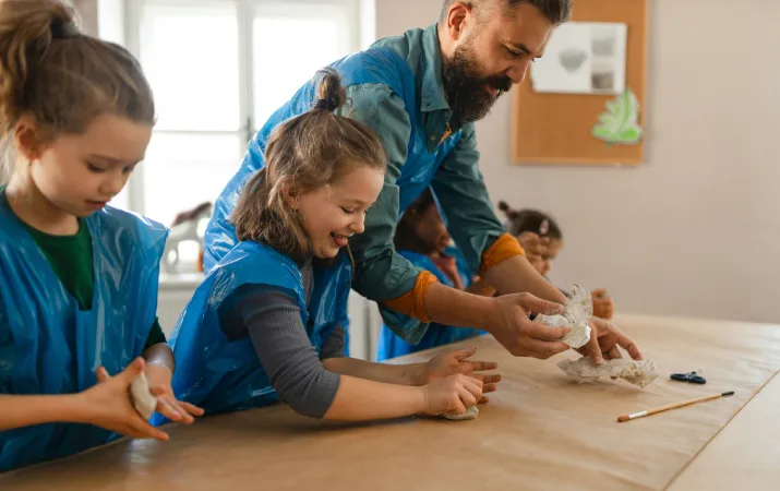A part-time art teacher showing primary school students how to model with clay