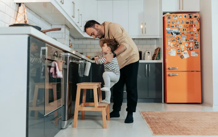 A dad taking a study break to care for his toddler in the kitchen of his house