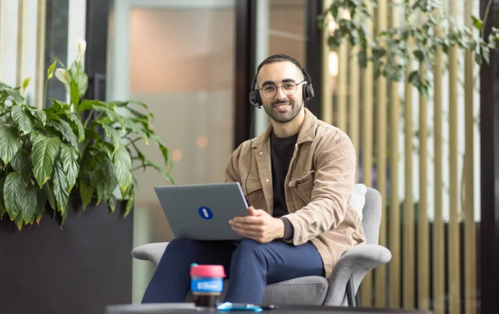 A smiling man wearing a headset with his laptop at the ready