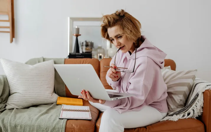 Woman chewing glasses while comparing courses on her laptop