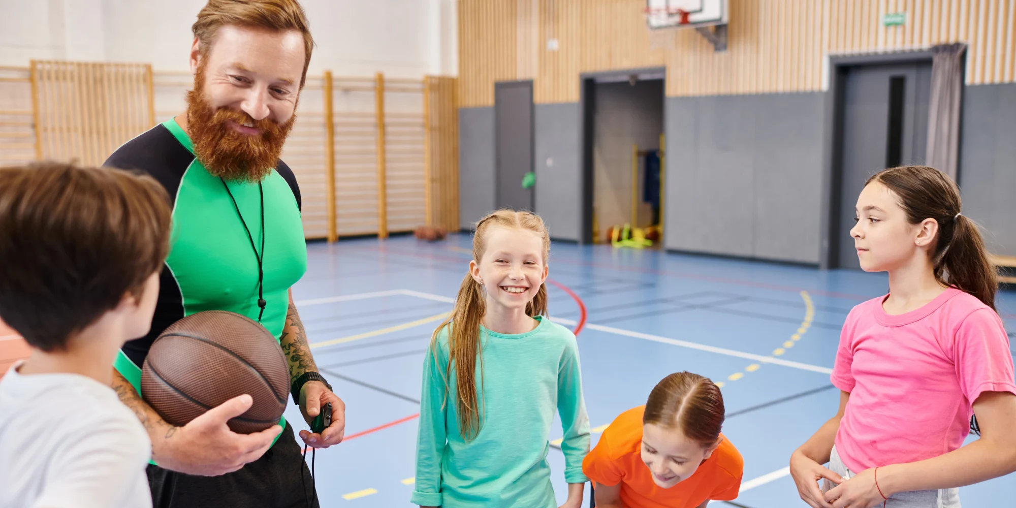 A male primary school teacher coaching his students inside a gym during a sports day
