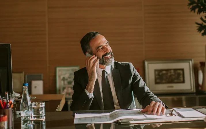 A man speaking on the phone while reviewing documents at an office desk.