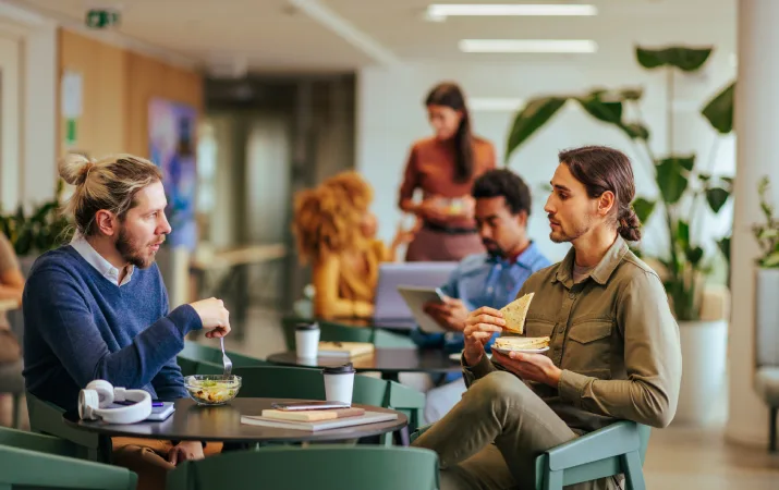 Two male teachers supporting each other and chatting during their lunch break in the staff room