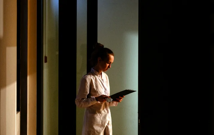 Person in a white coat reviewing a clipboard in a dimly lit setting.