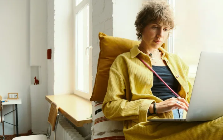 Person using a laptop while seated beside a window.