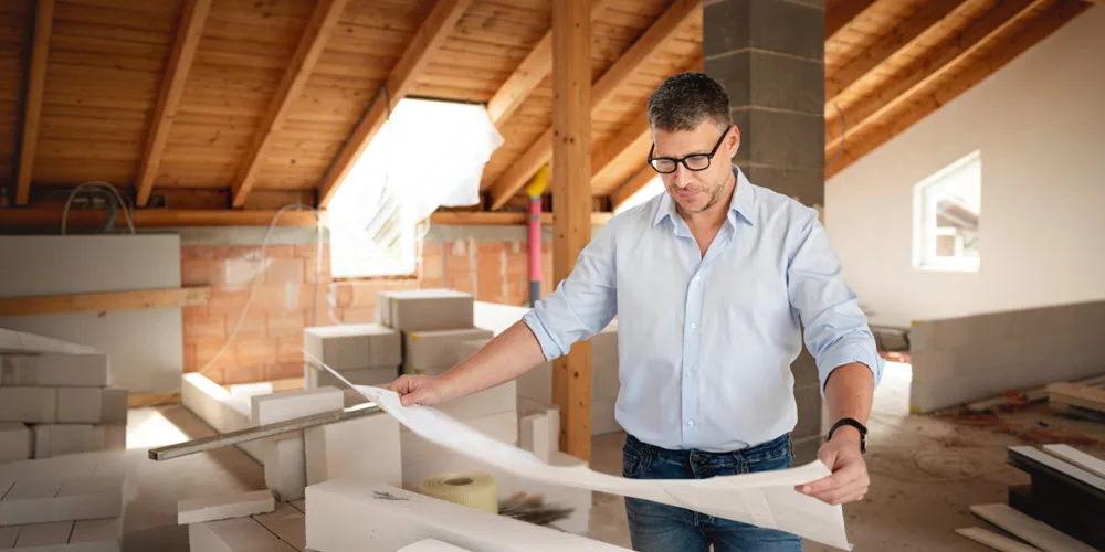 An architect in a brightly lit building site looking at drawings.