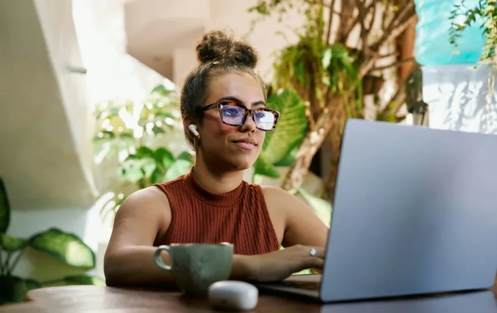 A woman in an outdoor cafe browsing low commitment psychology courses on her laptop and smiling
