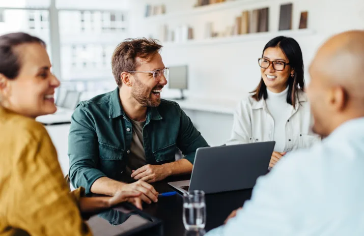 A group of four people smiling and chatting around a laptop