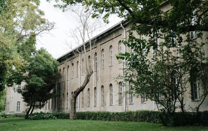 A stone university building surrounded by green lawn and trees