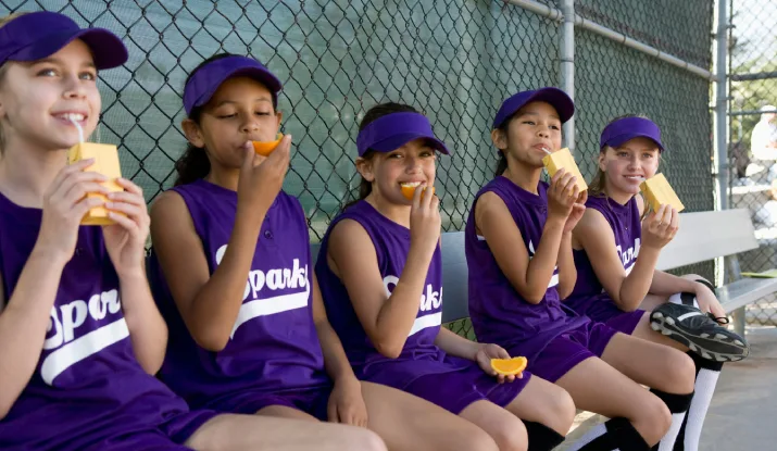 Primary school students drinking and eating during a break from a softball game