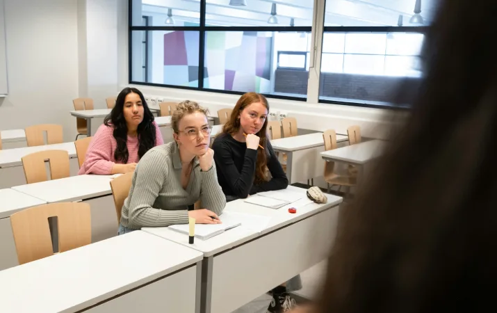 Three TAFE students staring attentively at their teacher in a classroom