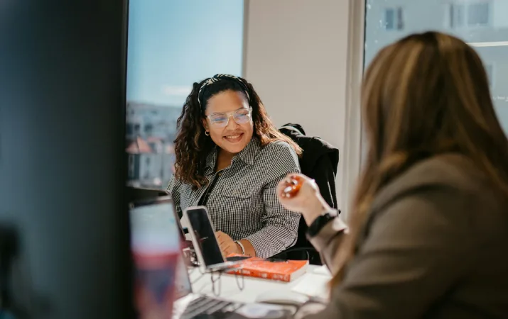 Two people discussing work across a desk in an office.