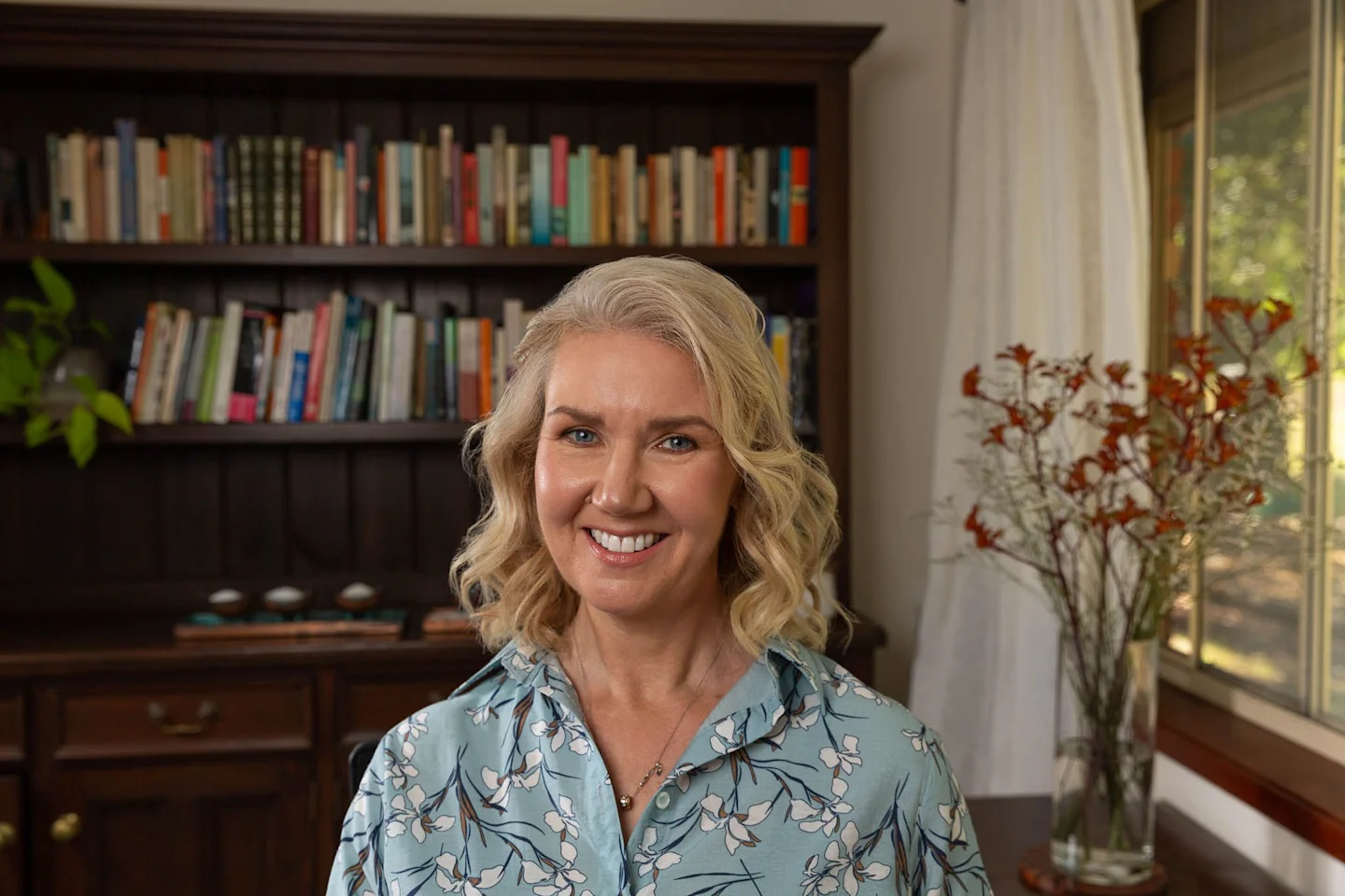 A warm blonde woman smiling in her home library