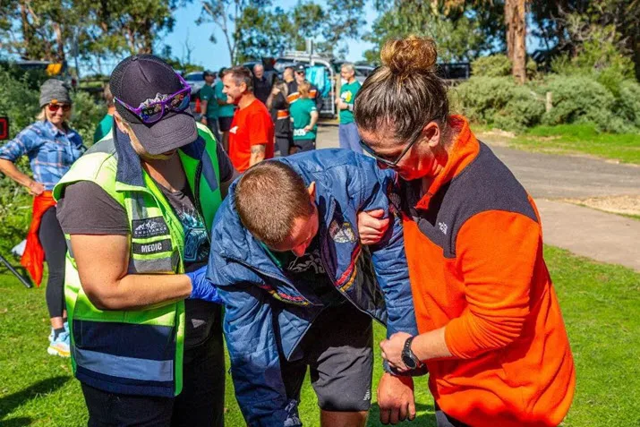Registered nurse Manna McLeod and another person helping an unwell athlete outside on a sunny day