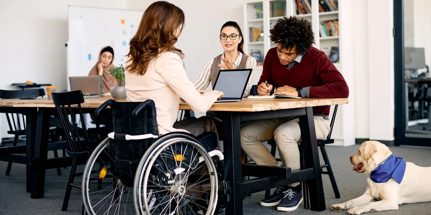 Community services professionals, customers, and an assistant dog collaborating in a community centre.