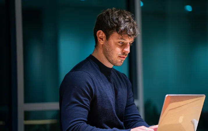 Man working on a laptop at a desk in an office at night.