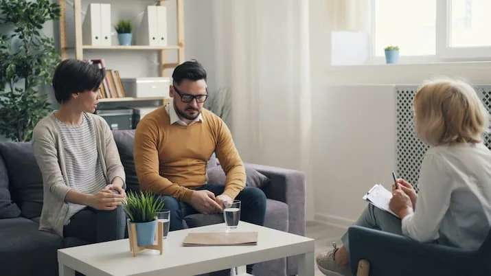 Woman and man seated on counselling couch speak with counsellor.
