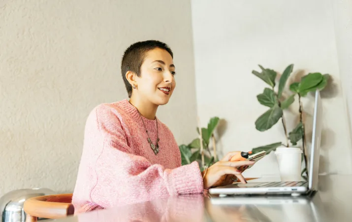 A smiling young honours student studying on her laptop in a bright office