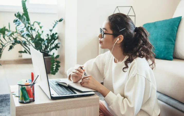 Female with earphones using a laptop and notebook at home.