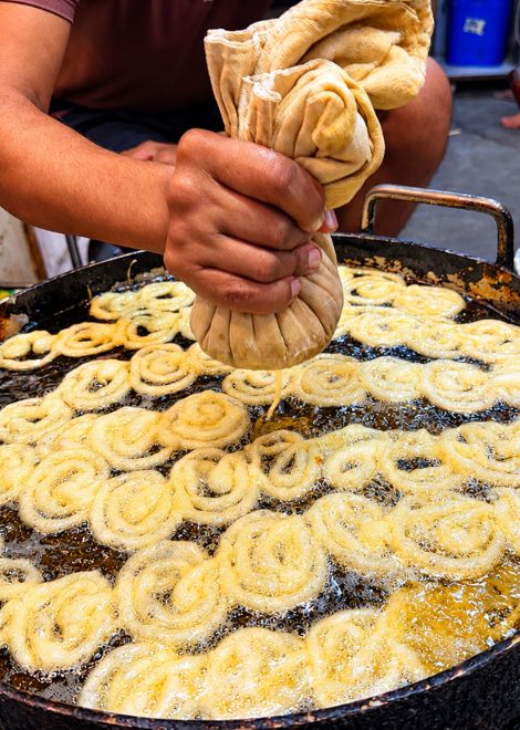 Jalebi batter swirled into hot oil in hypnotic spirals.