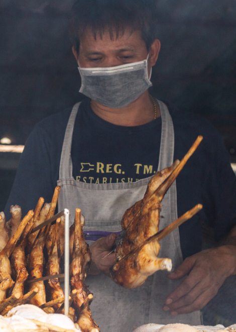 Spatchcocked gai yang chicken cooking over hot coals