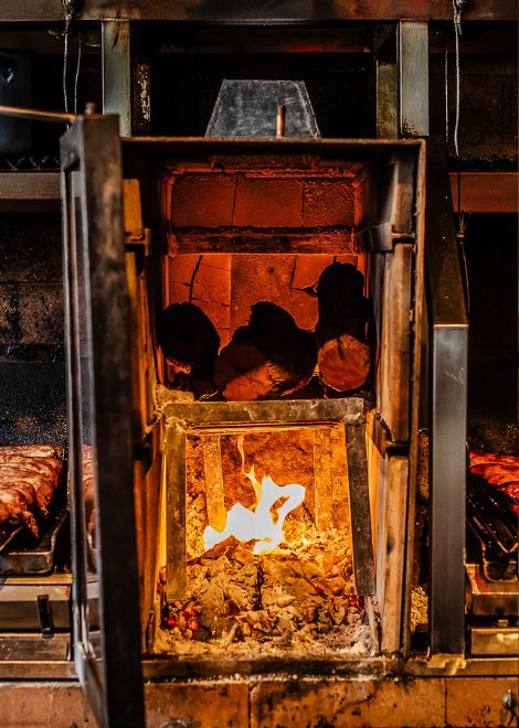 Flames crackle beneath the grill as chimichurri sausages sizzle over open coals