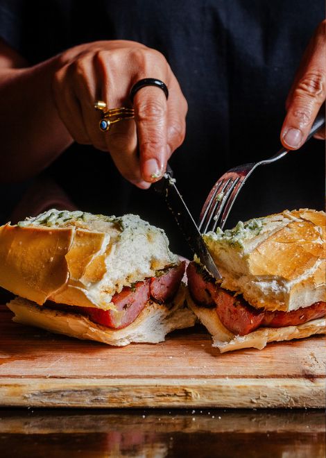 A freshly grilled sausage tucked into a crusty roll and topped with vibrant chimichurri