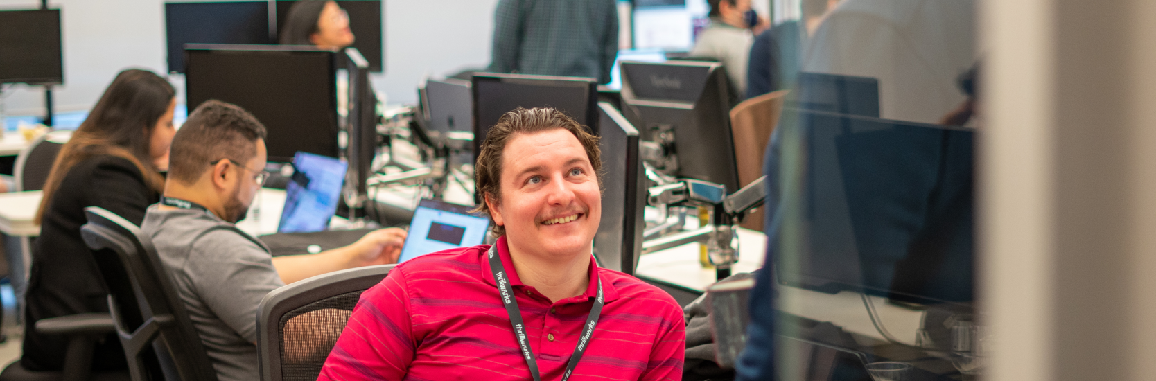 Man sitting at desk in tech office smiling at colleague