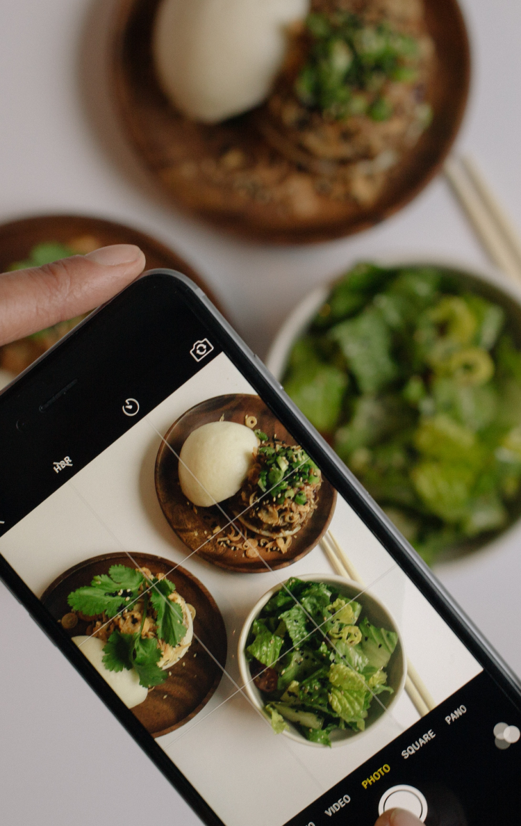 A woman takes a photo of food on a countertop with a mobile phone.