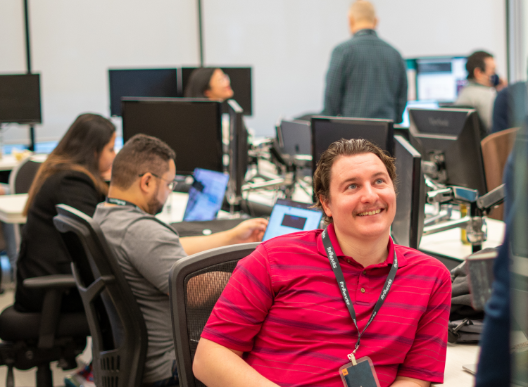 Man sitting at desk in tech office smiling at colleague