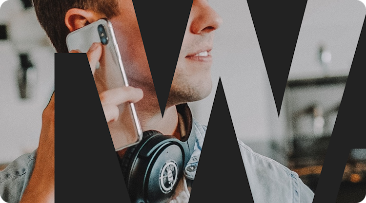 A knockout text effect showing a man working at a desk, wearing headphones around his neck while using a mobile phone.