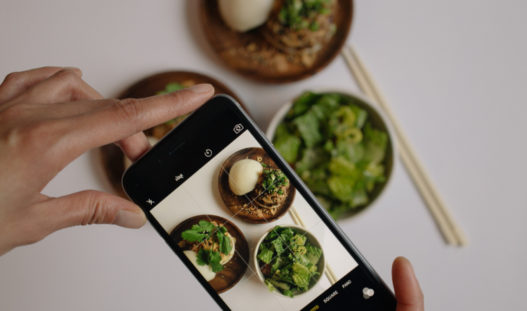 A woman takes a photo of food on a countertop with a mobile phone.
