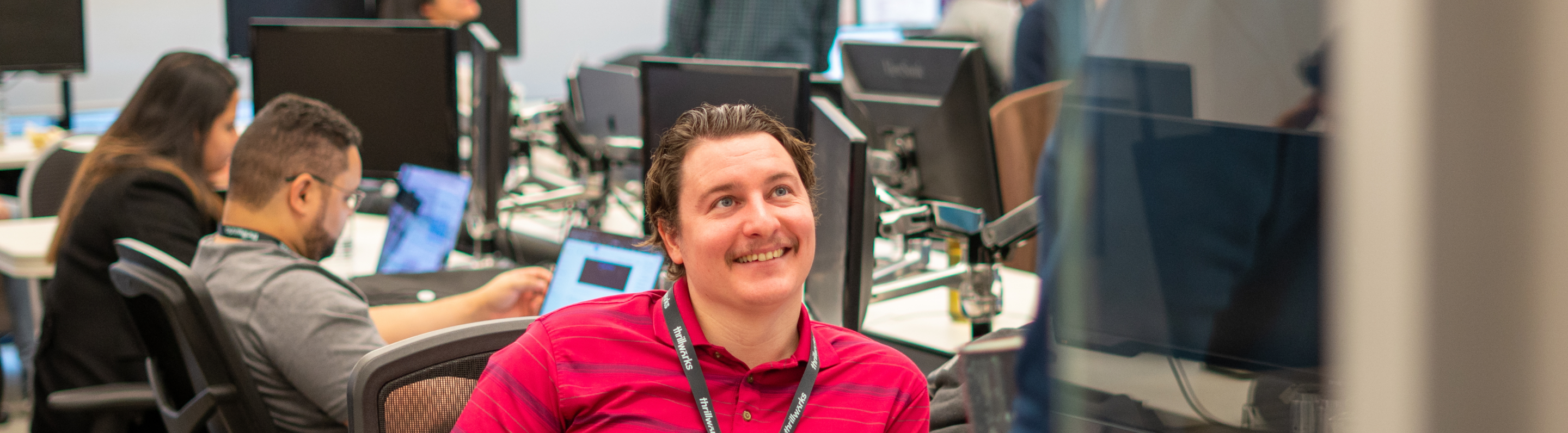 Man sitting at desk in tech office smiling at colleague
